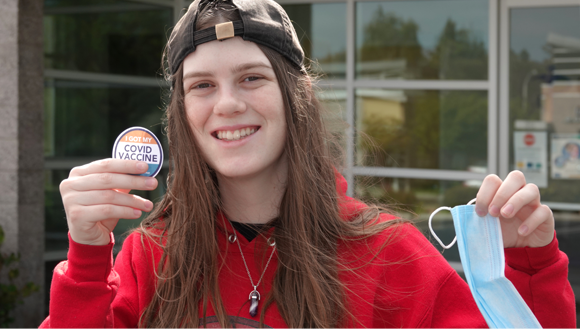 נערה מחייכת מחזיקה מדבקה של החיסון ומורידה מסכה | Shutterstock, Simone Hogan