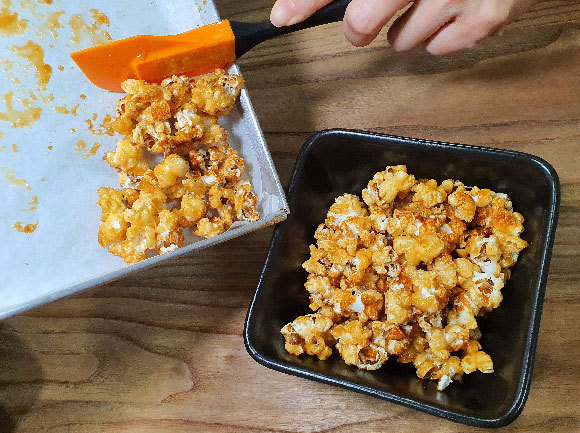 Transferring the baked caramel popcorn from the oven tray to a serving dish | Photo: Toshio Chan, Shutterstock