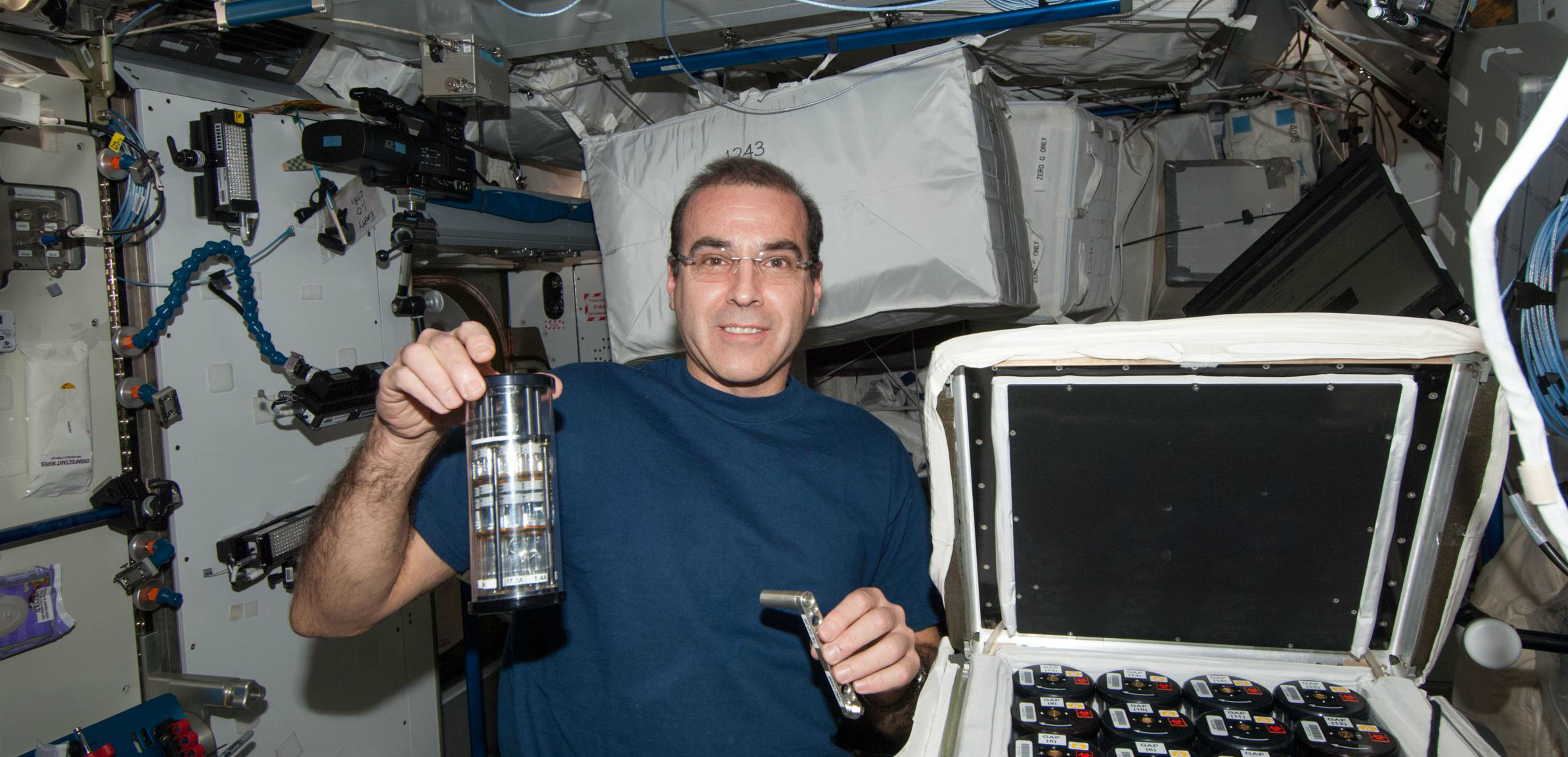 האסטרונאוט ריק מסטרקיו עם אחד ממכלי הגידול של החיידקים, ליד האינקובטור | צילום מתוך מאמר המחקר