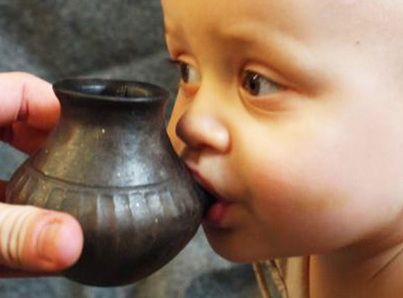 תינוק שותה מרפליקה של בקבוק חרס עתיק | Helena Seidl da Fonseca