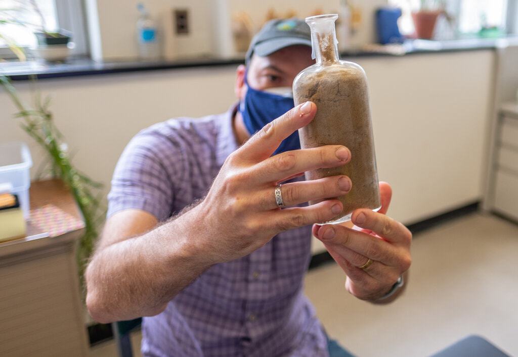 החוקר דיוויד לורי (Lowry) עם בקבוק זרעים שהוצא מהאדמה | צילום: דרק ל' טרנר, אוניברסיטת מישיגן סטייט