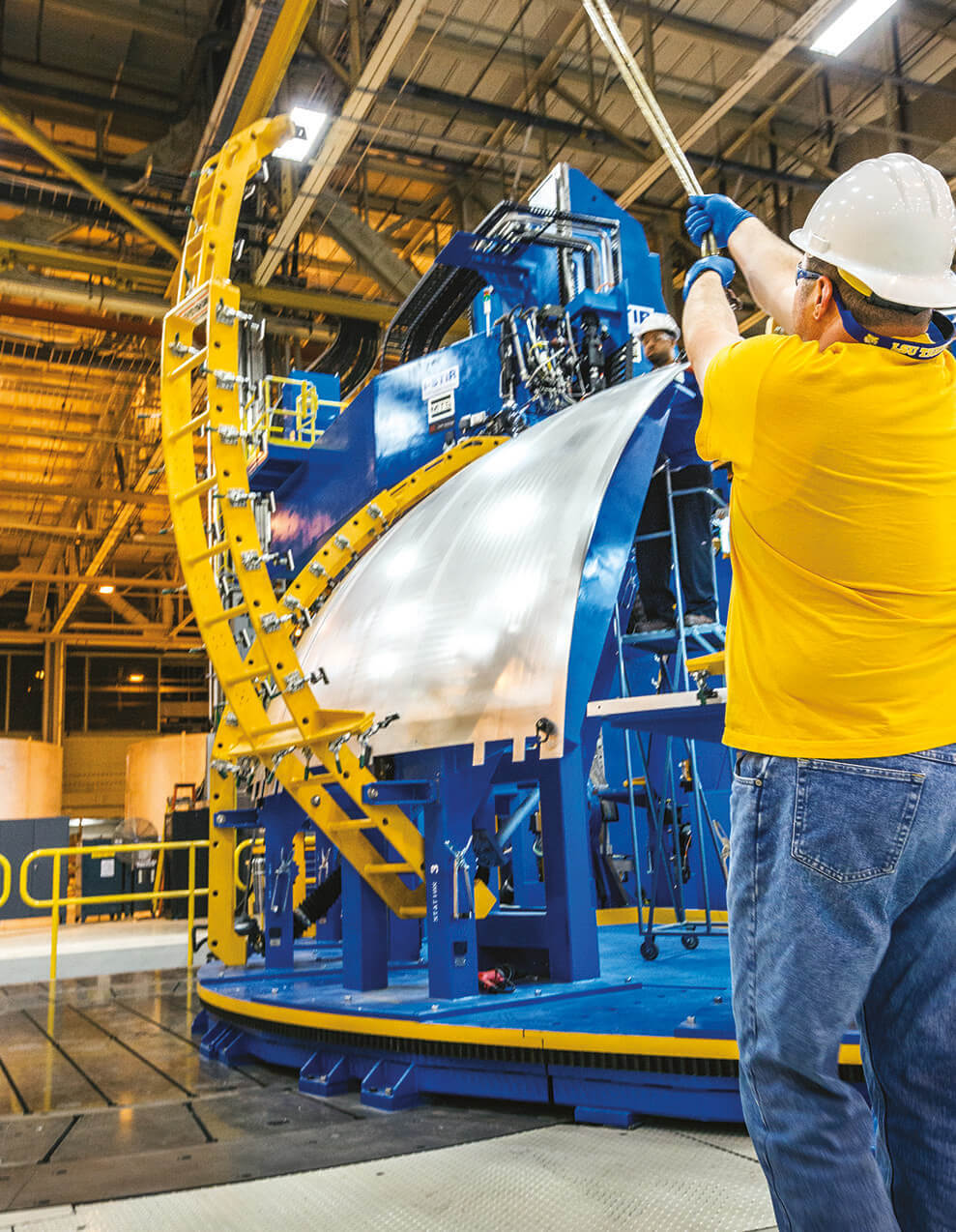 עובדים מרימים לוח אלומיניום אל כלי שמשמש להרכבת הכיסוי דמוי הכיפה של שלב הליבה. 